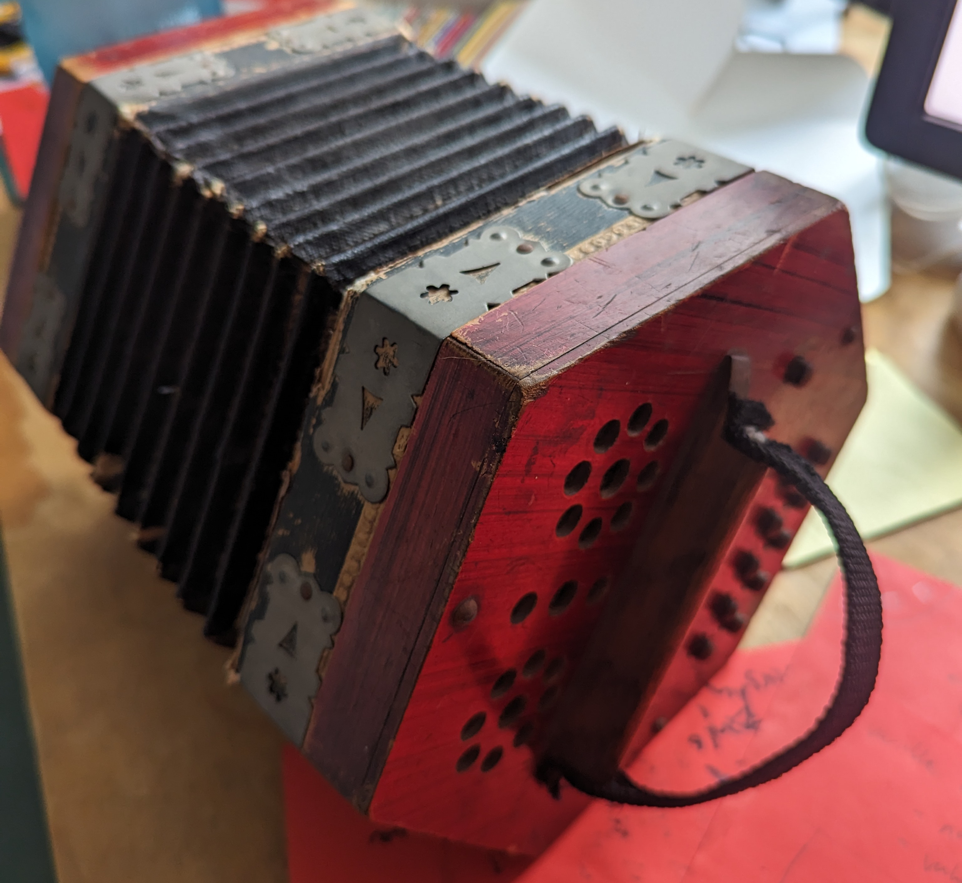 The battered concertina before restoration, with its worn red body and leaking bellows.